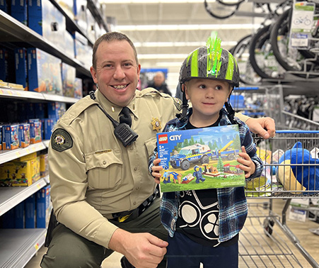 Matt Roberts with a kid holding a LEGO police car at Shop with a Cop 2023