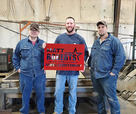 Matt Roberts holding a custom sign with 2 J&S welding employees