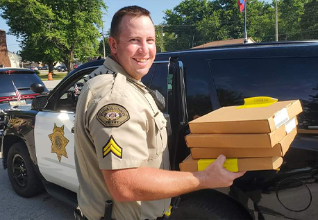 Matt Roberts carrying boxes while standing in front of his HCSO patrol car